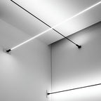 Two Clérachic strip lights cross in the corner of a white room, one lit and one black, each held by a wall bracket.