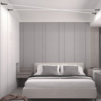 A Clérachic strip light crosses the ceiling above a bed with grey headboard panels, in a pale grey bedroom.