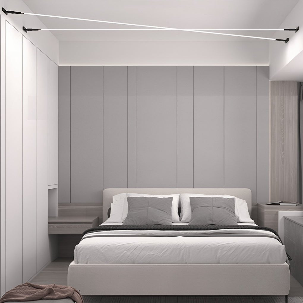 A Clérachic strip light crosses the ceiling above a bed with grey headboard panels, in a pale grey bedroom.