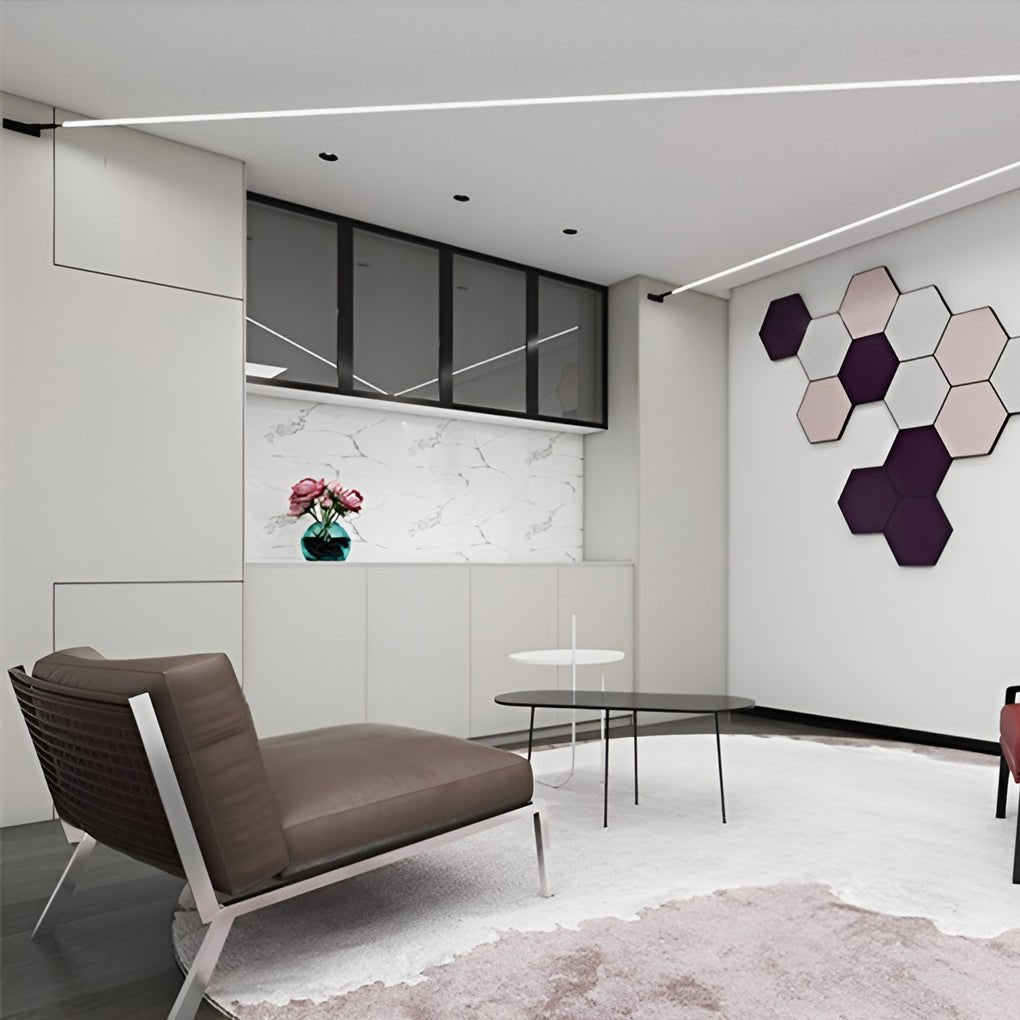 A Clérachic strip light crosses the ceiling of a living area with a brown lounge chair and hexagonal pink-and-plum wall tiles.