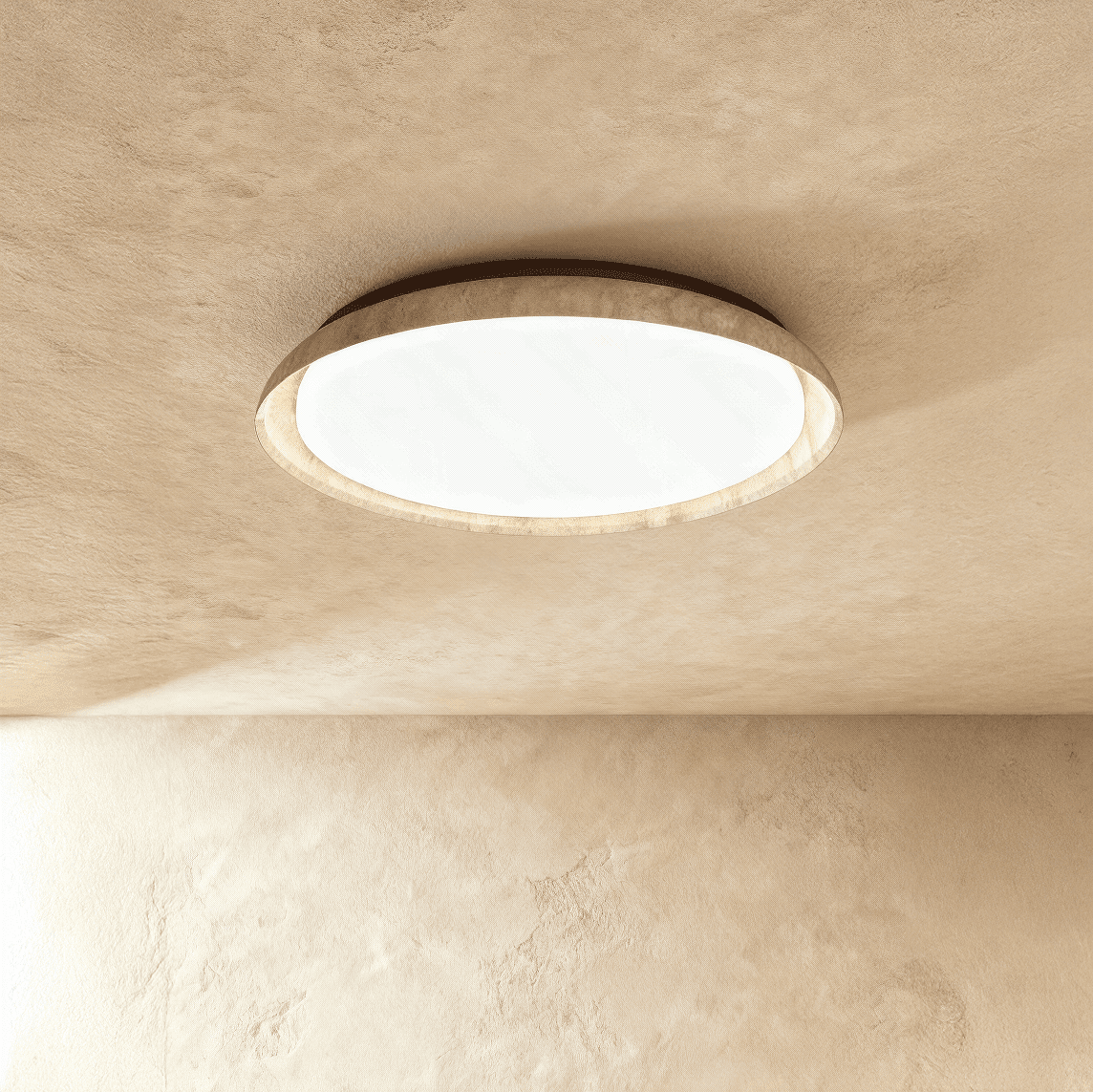 Clérachic flat round ceiling light with a travertine-look ring and white diffuser, mounted on a textured sand-toned plaster ceiling.