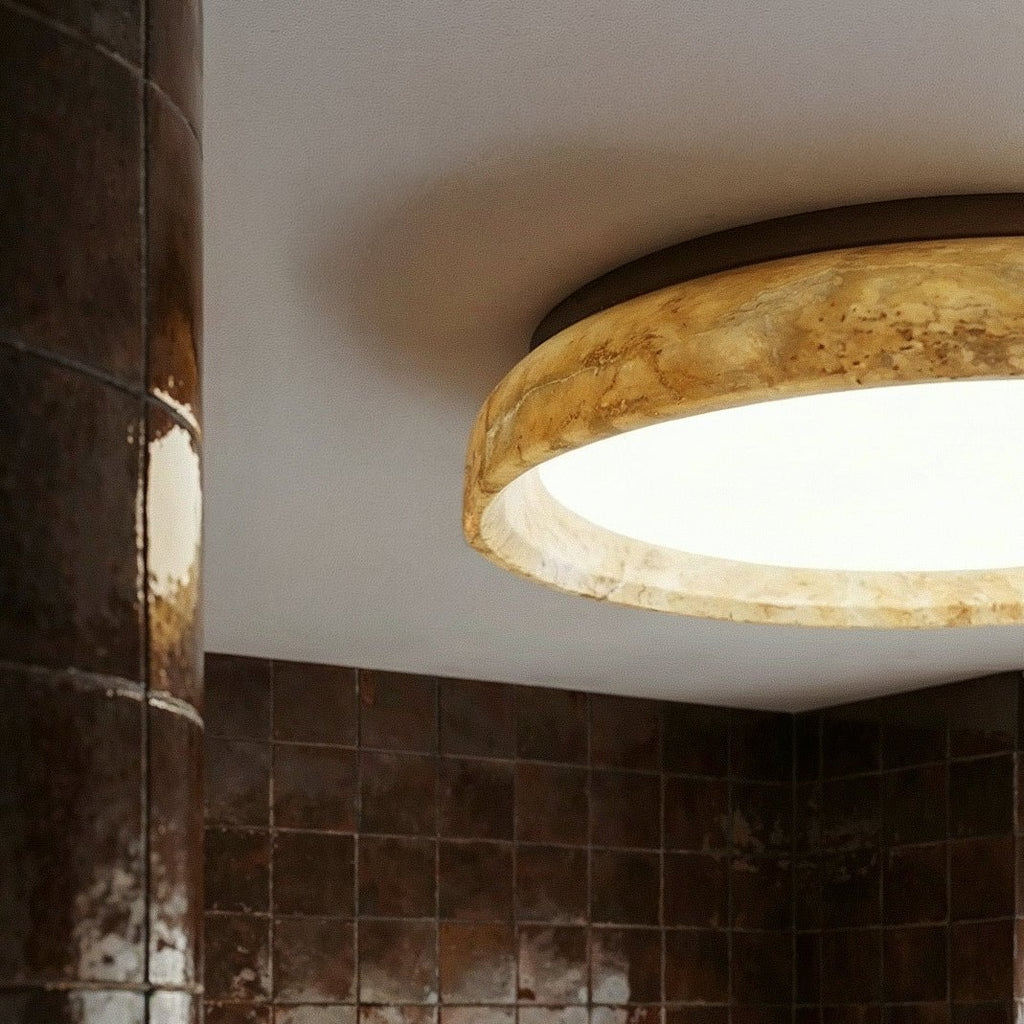 Close view of the Clérachic ceiling light's honey-veined stone-look ring and bright white diffuser, lit against a white ceiling.