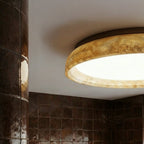 Close view of the Clérachic ceiling light's honey-veined stone-look ring and bright white diffuser, lit against a white ceiling.
