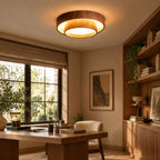 A Clérachic wood-grain ceiling light above a home office with a wooden desk, a window with a woven blind and built-in shelves of books.