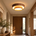 Lit Clérachic ceiling light in an entrance hall with a solid wooden front door, an arched niche and a large vase of foliage.