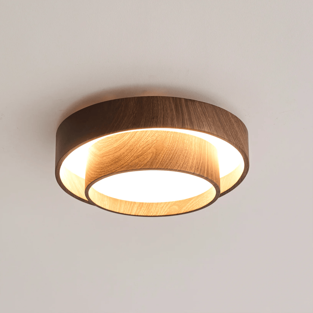 Lit Clérachic ceiling light on a pale ceiling, its light-oak-toned inner faces glowing warm between two walnut wood-grain rings.