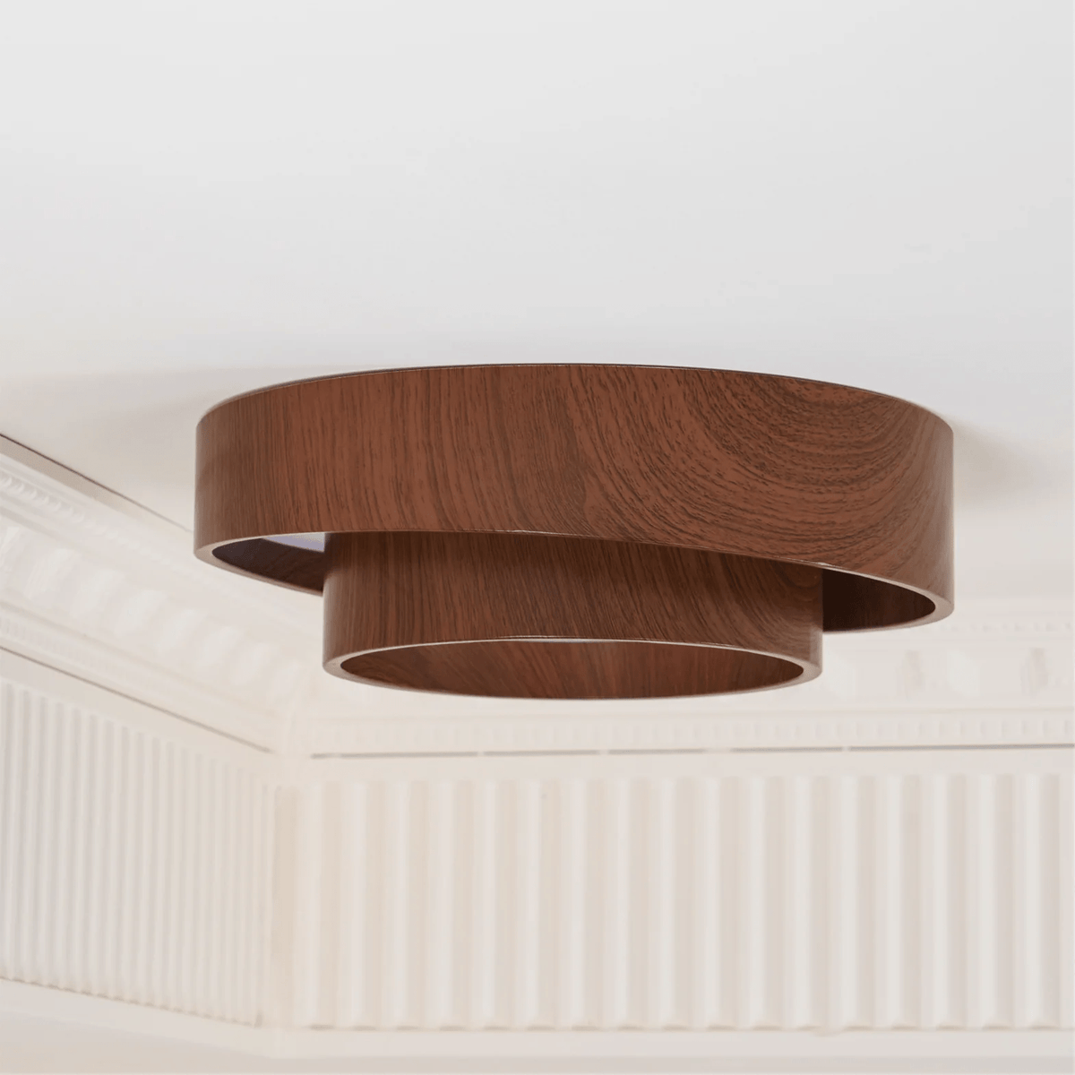 Side view of an unlit Clérachic ceiling light with two stacked walnut-look rings, against a ceiling with white cornice moulding.