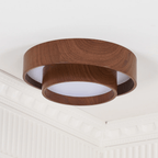 Clérachic wood-grain ceiling light seen from below at an angle, with a white diffuser and ornate white cornice behind.