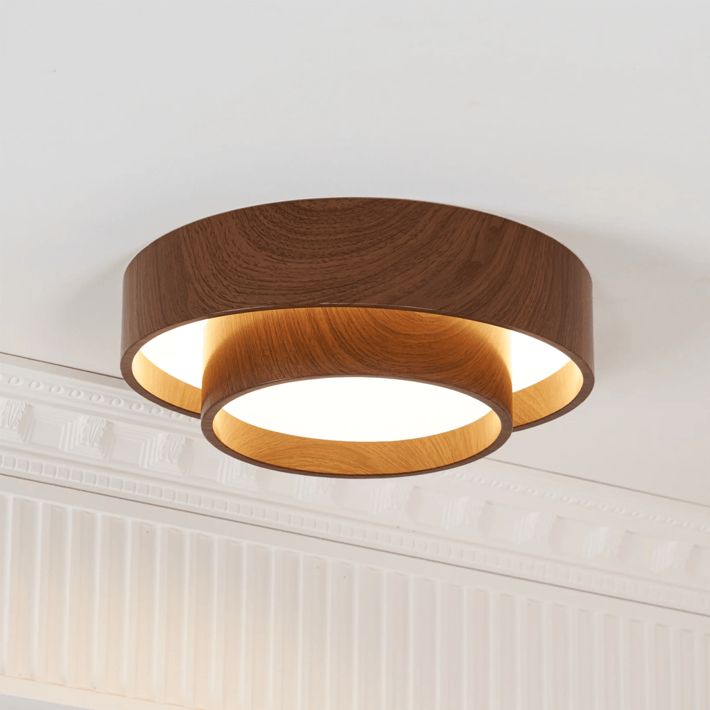 Lit Clérachic ceiling light with a warm glow inside its lower ring, set against a white ceiling with decorative cornice.