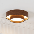 Lit Clérachic ceiling light with a warm glow inside its lower ring, set against a white ceiling with decorative cornice.