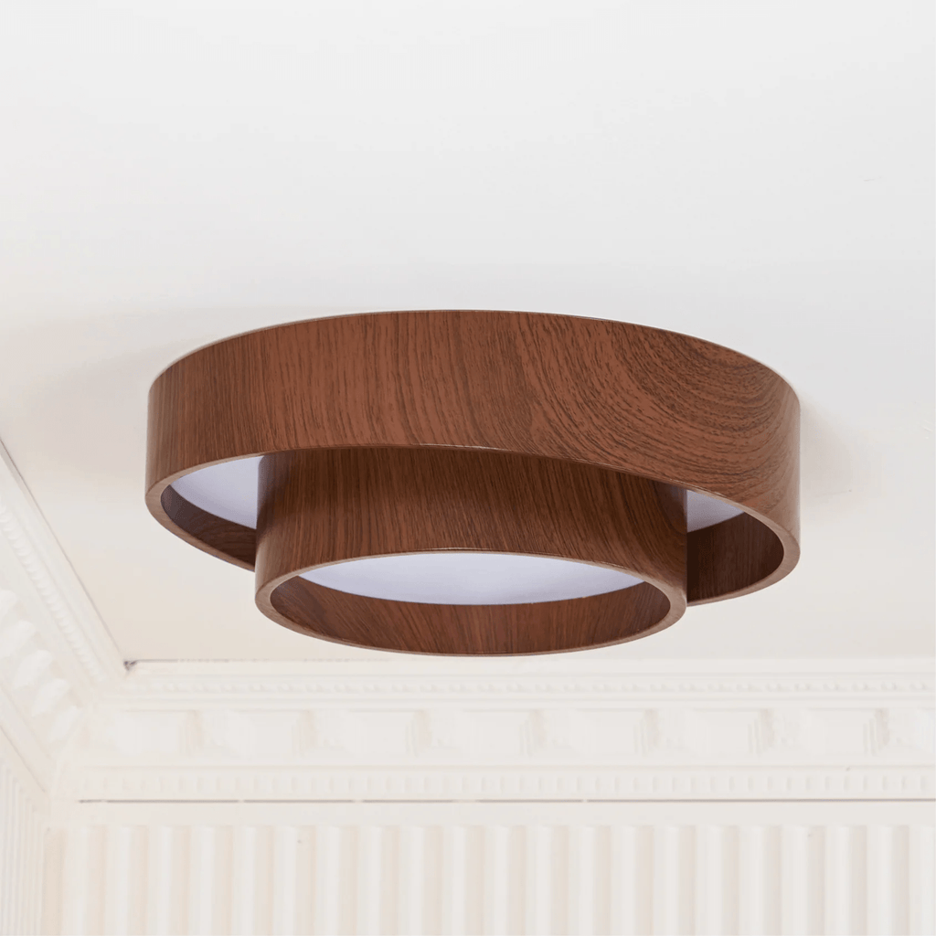 Unlit Clérachic ceiling light with two wood-grain rings, near a white corner with detailed cornice and fluted wall panelling.