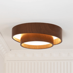 A Clérachic ceiling light glowing amber between its stacked rings, beside a white cornice and fluted wall.