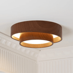 Clérachic flush light, lit, with an upper walnut-look ring over a warm-glowing lower ring, in a room with a plaster cornice.