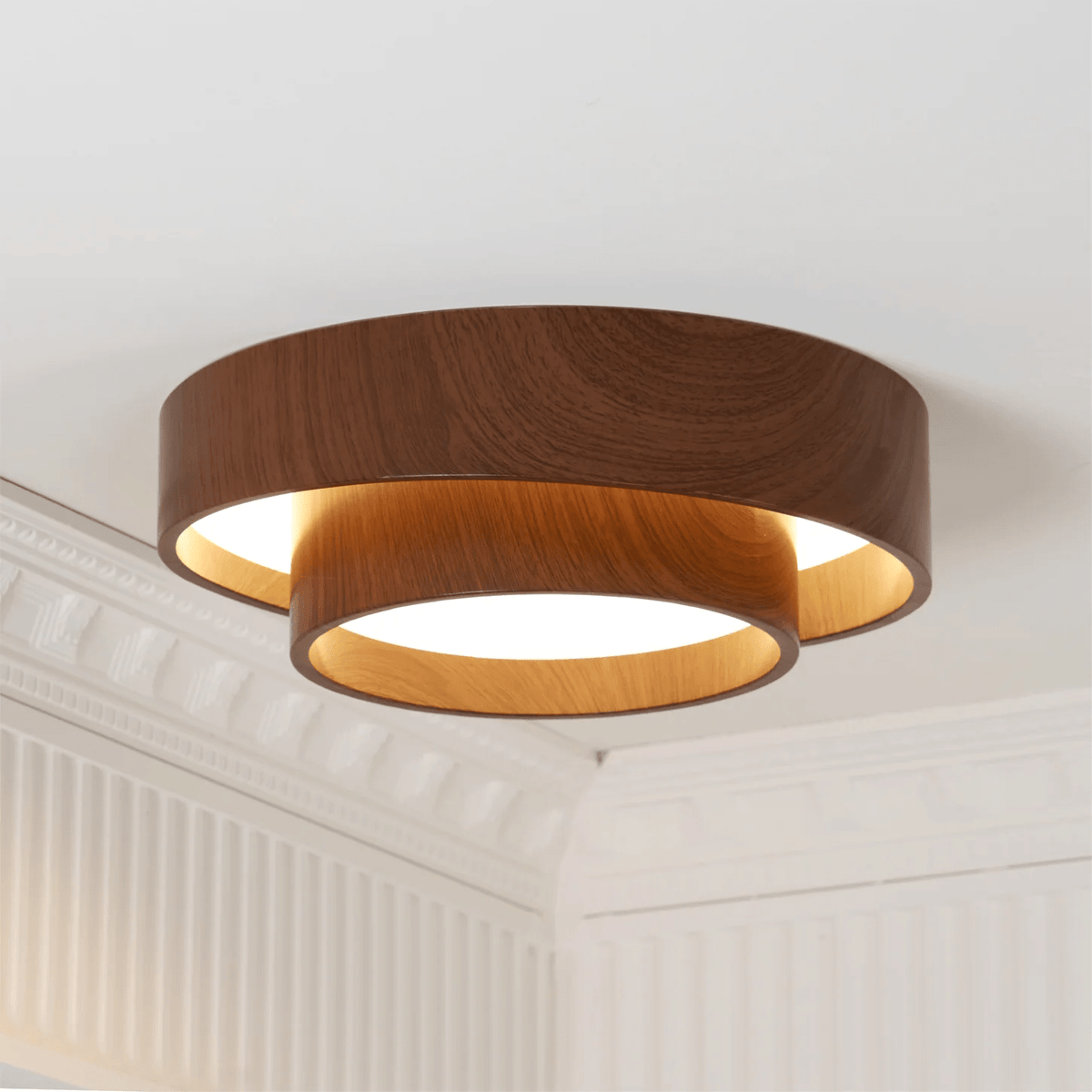 Clérachic flush light, lit, with an upper walnut-look ring over a warm-glowing lower ring, in a room with a plaster cornice.