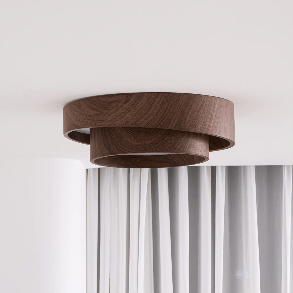 Side view of a Clérachic ceiling light with two stepped wood-grain rings, hung over white curtains on a pale wall.