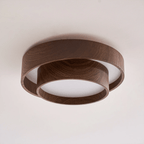 Clérachic ceiling light seen from a low angle on a pale ceiling, with a thick walnut-look ring and a smaller ring below it.