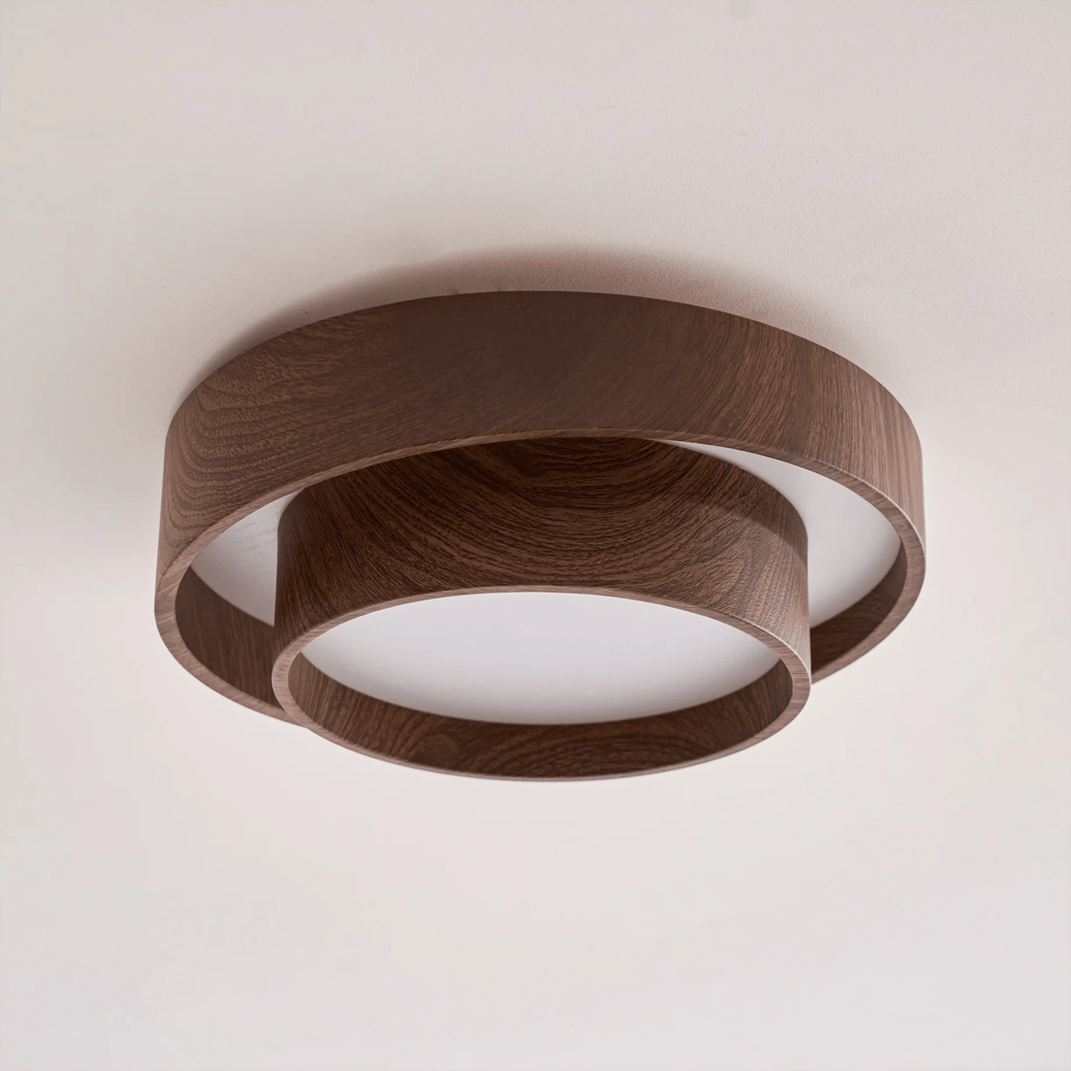 Clérachic ceiling light seen from a low angle on a pale ceiling, with a thick walnut-look ring and a smaller ring below it.