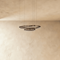 Clérachic two-ring LED chandelier in dark bronze-toned metal with wavy outlines, hung on thin cables against a plaster wall.
