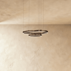 Clérachic two-ring LED chandelier in dark bronze-toned metal with wavy outlines, hung on thin cables against a plaster wall.