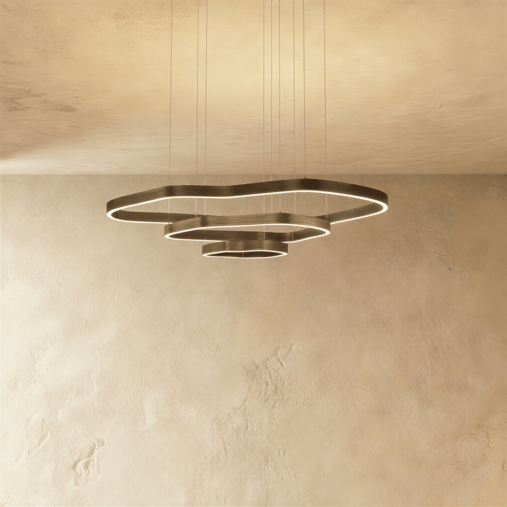 Clérachic wider three-ring LED chandelier, stepped wavy bronze rings with built-in light, hung on cables against plaster.