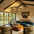 Clérachic two-ring chandelier in brushed brass hanging under a beamed vaulted ceiling above a curved blue sofa and burr-wood table.