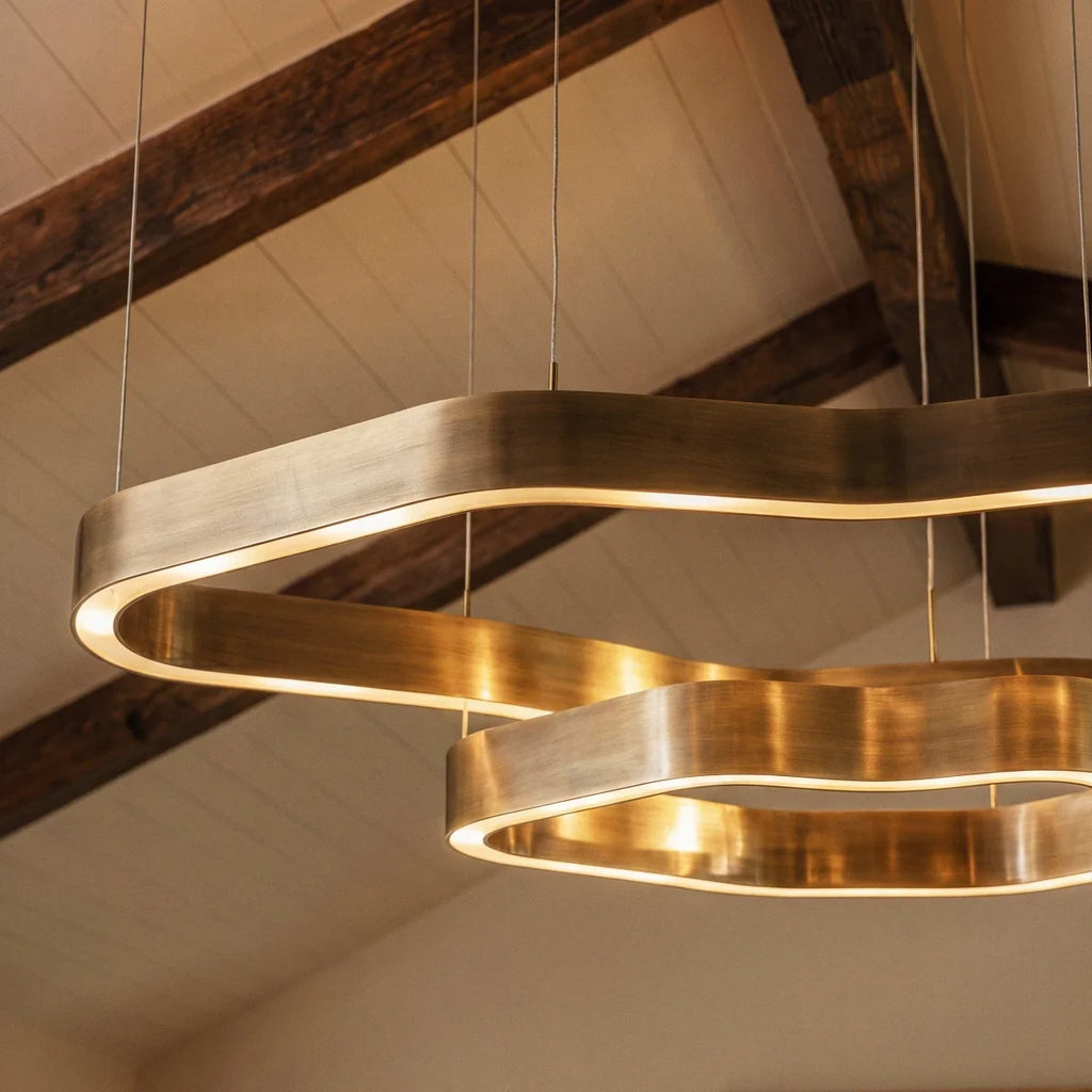 Close view of a Clérachic chandelier's brushed brass rings, a warm LED line running along the inner edge beneath timber beams.