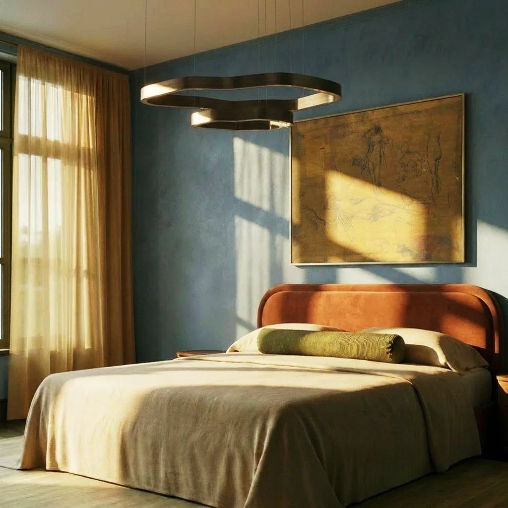 Clérachic two-ring chandelier in dark bronze above a bed with a rust headboard, against a blue plaster wall in low sun.