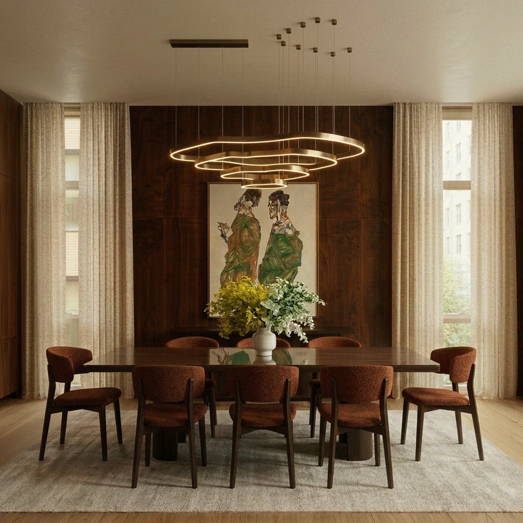 Clérachic four-ring brass LED chandelier hung over a long walnut dining table with rust-coloured chairs and a vase of flowers.