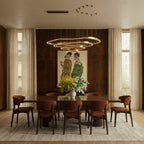 Clérachic four-ring brass LED chandelier hung over a long walnut dining table with rust-coloured chairs and a vase of flowers.