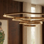 Close view of the four stacked wavy brass rings of a Clérachic chandelier, each lit along its inner edge, beside walnut panelling.
