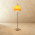 Clérachic floor lamp with a glowing orange glass dome on a slim chrome stem and round base, against a limewash wall.
