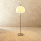 Clérachic floor lamp with a milky white glass dome glowing warm on a slim chrome stem and a flat round base.