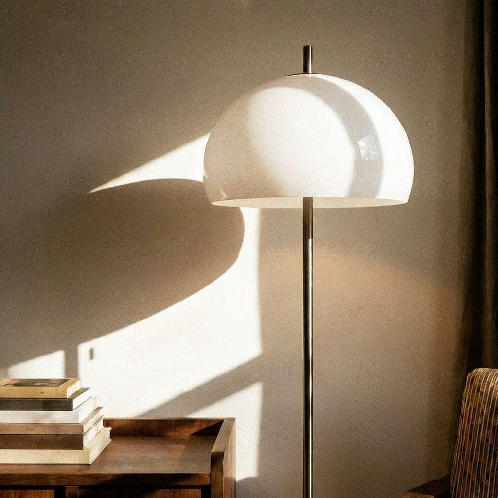 Clérachic floor lamp close up, a glossy white glass dome above a slim chrome stem, with soft light on the wall.