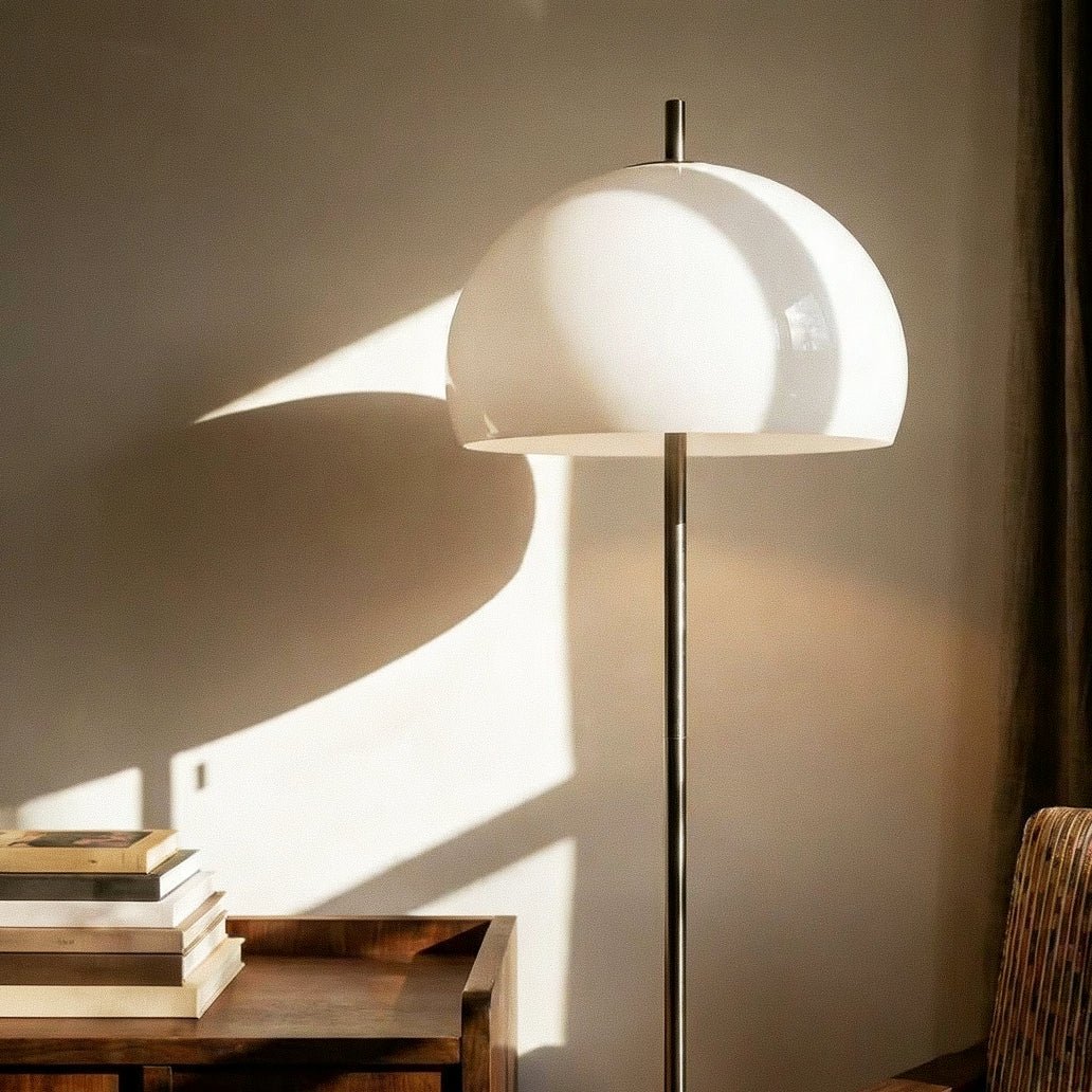 Clérachic floor lamp close up, a glossy white glass dome above a slim chrome stem, with soft light on the wall.
