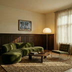 Clérachic floor lamp with a white glass dome and chrome stem beside a green velvet sofa and a sheer-curtained window.