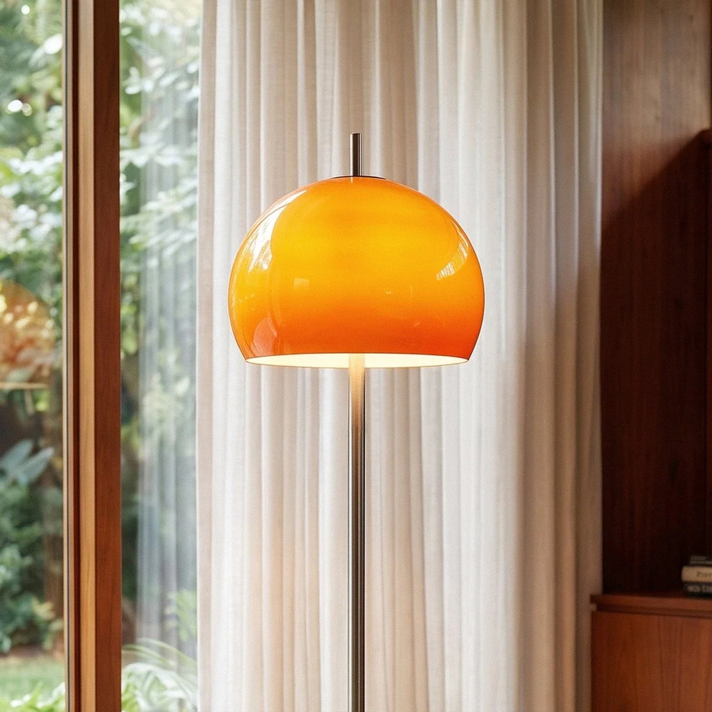 Clérachic floor lamp close up, a glossy orange glass dome glowing from within above a slim chrome stem.
