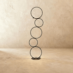 Clérachic floor lamp of five stacked black LED rings glowing warm white on a round base, studio shot against a limewash wall.