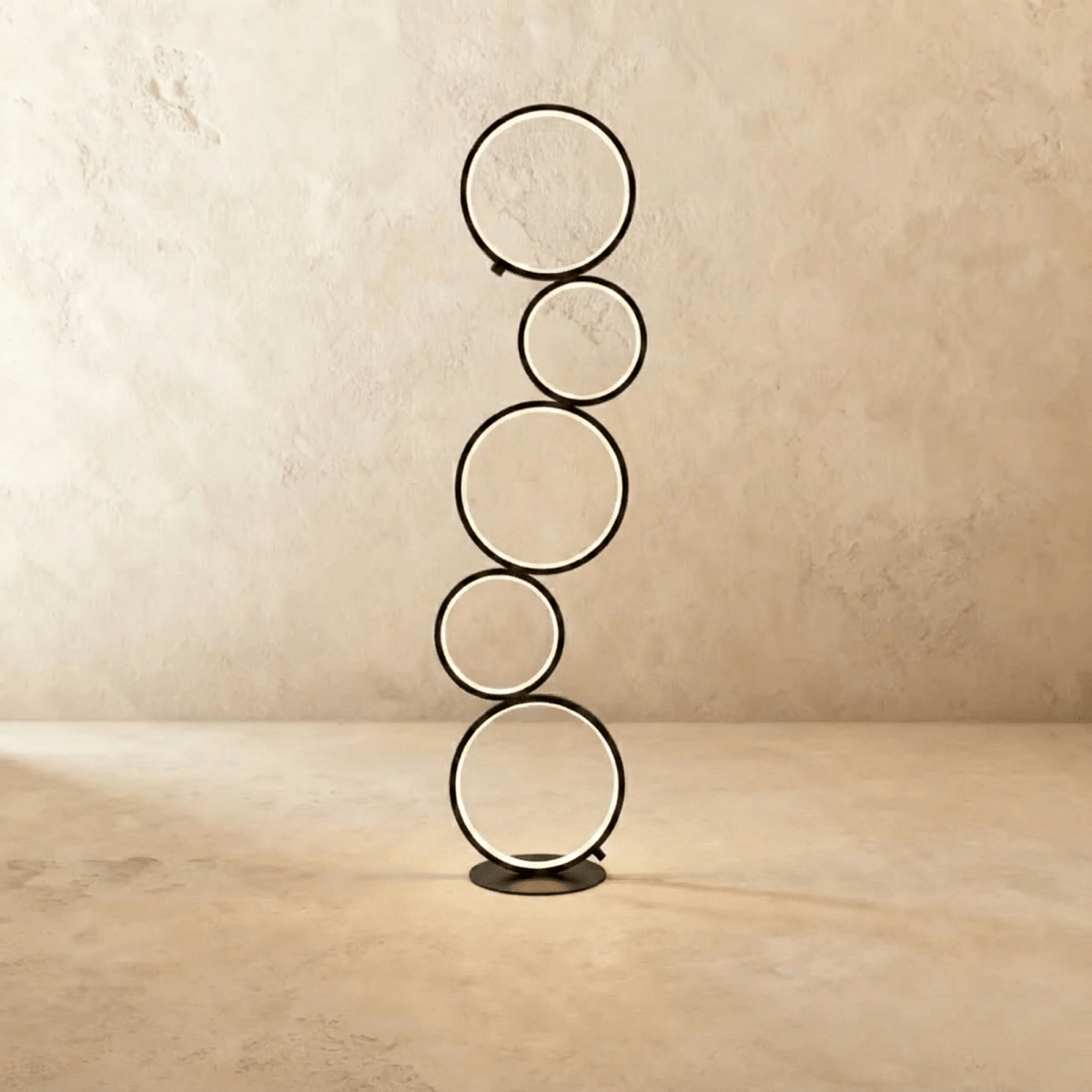 Clérachic floor lamp of five stacked black LED rings glowing warm white on a round base, studio shot against a limewash wall.