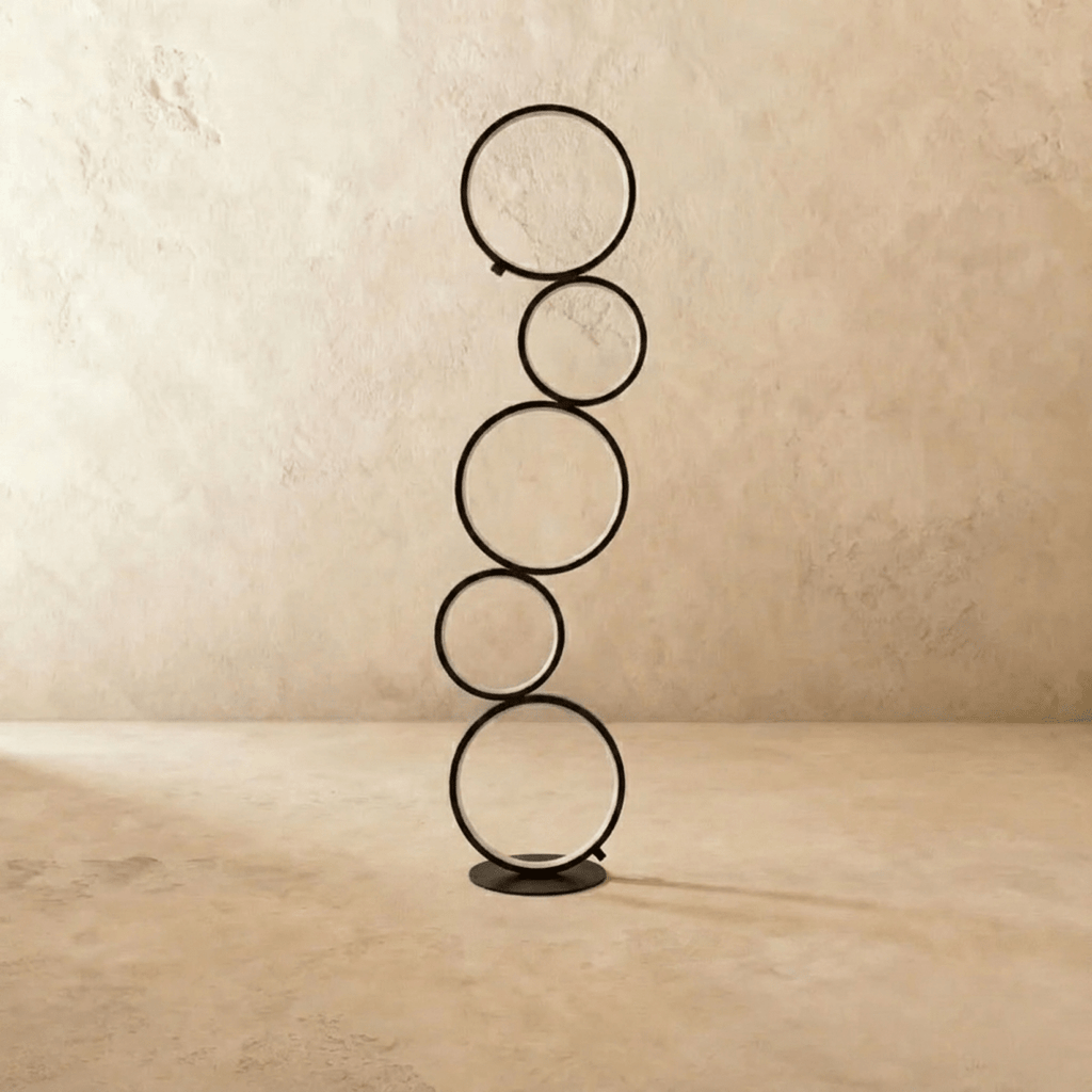Clérachic floor lamp of five stacked black rings switched off, standing on a round black base in a plain studio setting.