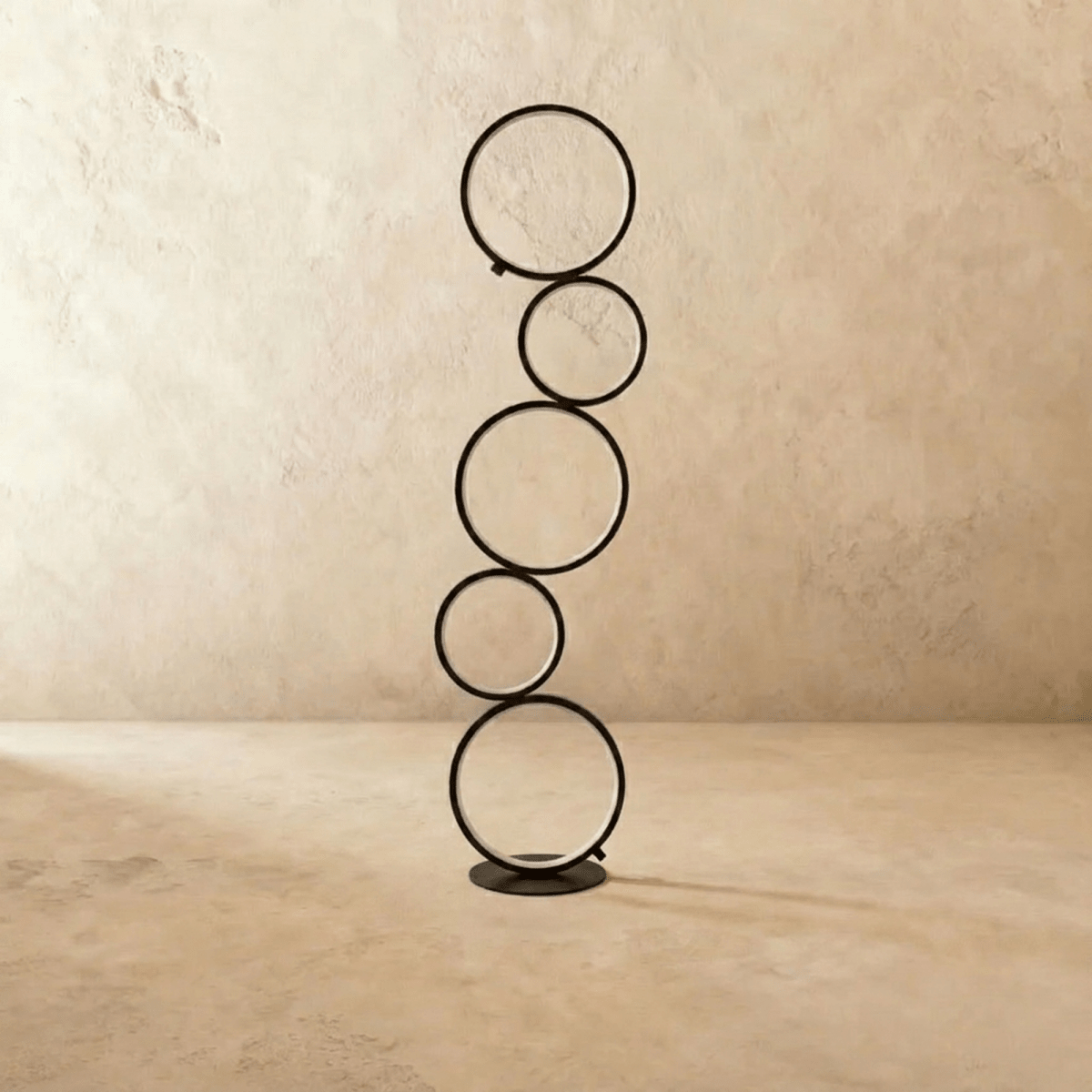 Clérachic floor lamp of five stacked black rings switched off, standing on a round black base in a plain studio setting.