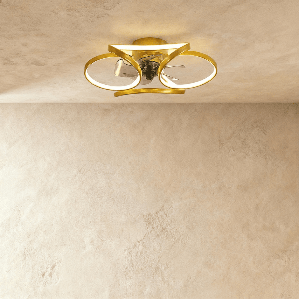 Clérachic ceiling fan with a light in gold, looped LED bands glowing warm around a small central fan in a studio.