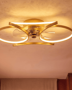 Close up of the Clérachic gold ceiling fan with a light, its looped LED bands glowing warm round the clear fan blades.