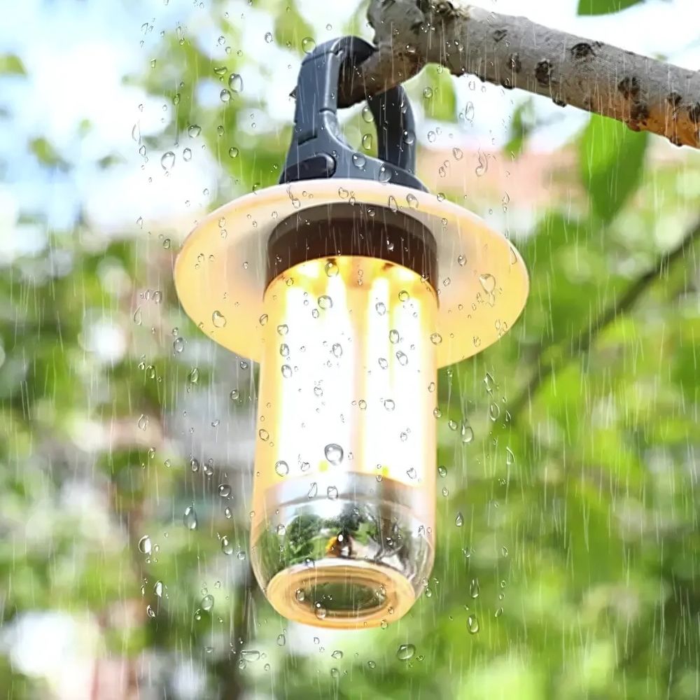 Clérachic tent lantern hanging from a wet branch in rain, water beading on the clear cylinder.
