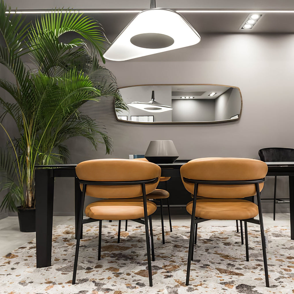 A white disc pendant with a dark centre hangs above a black dining table with tan leather chairs and a tall palm, from Clérachic.