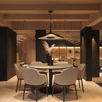 A black disc pendant hangs over a round marble dining table with cream chairs, in a warm timber-ceilinged room, a Clérachic LED pendant.