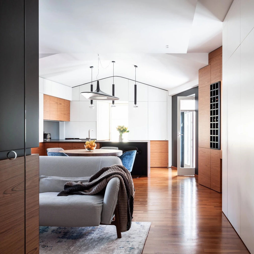 Three pendants, one of them a black disc, hang in an open kitchen and living area with a vaulted ceiling and a grey sofa, from Clérachic.