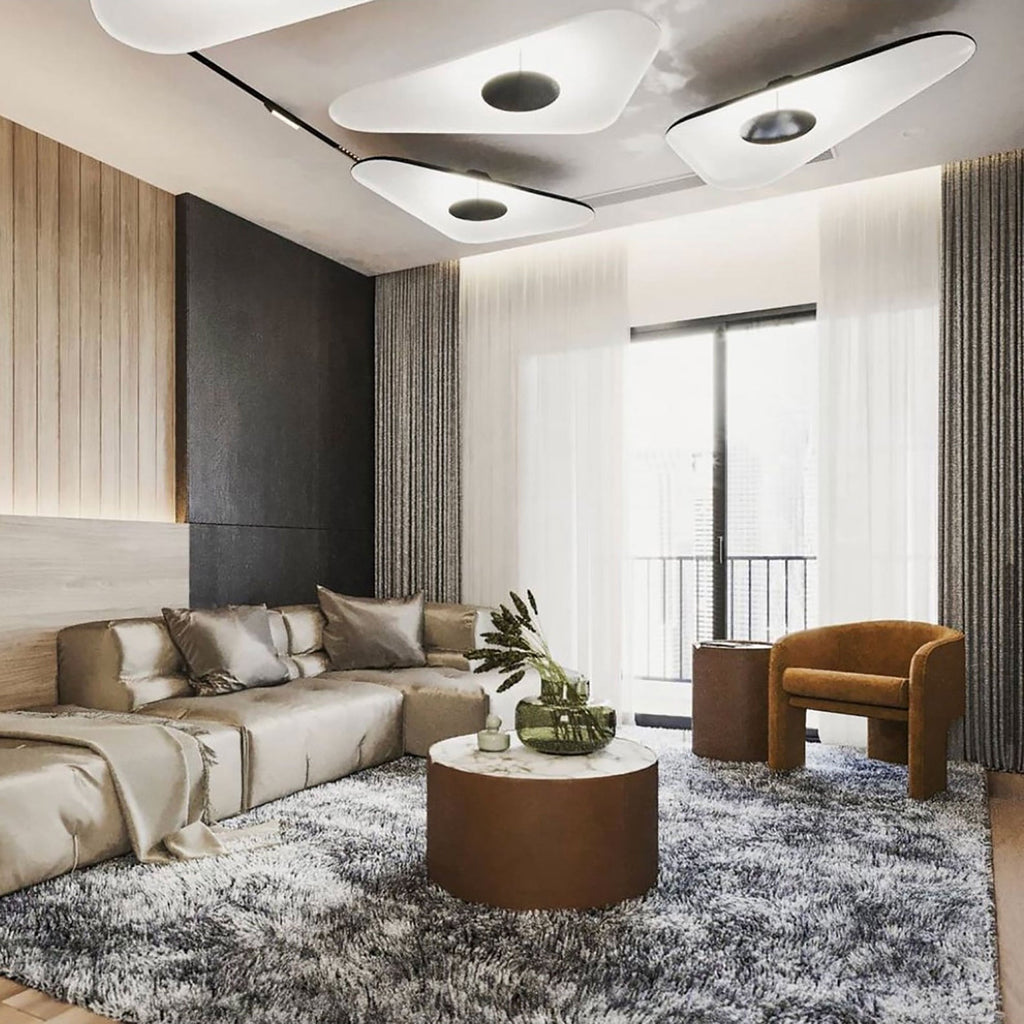 Three white disc pendants glow overhead in a living room with a cream corner sofa, a round table and sheer curtains, from Clérachic.