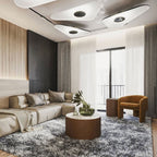 Three white disc pendants glow overhead in a living room with a cream corner sofa, a round table and sheer curtains, from Clérachic.