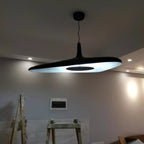 A black disc pendant lit from below hangs from a round black canopy in a grey room still under construction, a Clérachic LED pendant.