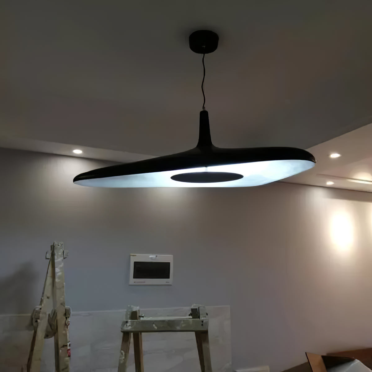 A black disc pendant lit from below hangs from a round black canopy in a grey room still under construction, a Clérachic LED pendant.